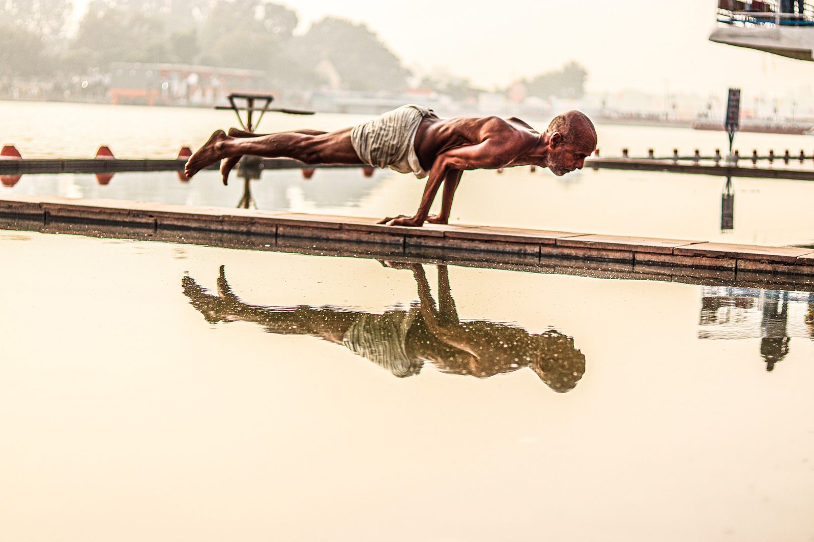 An older man holding a plank pose on a dock, reflected in the water