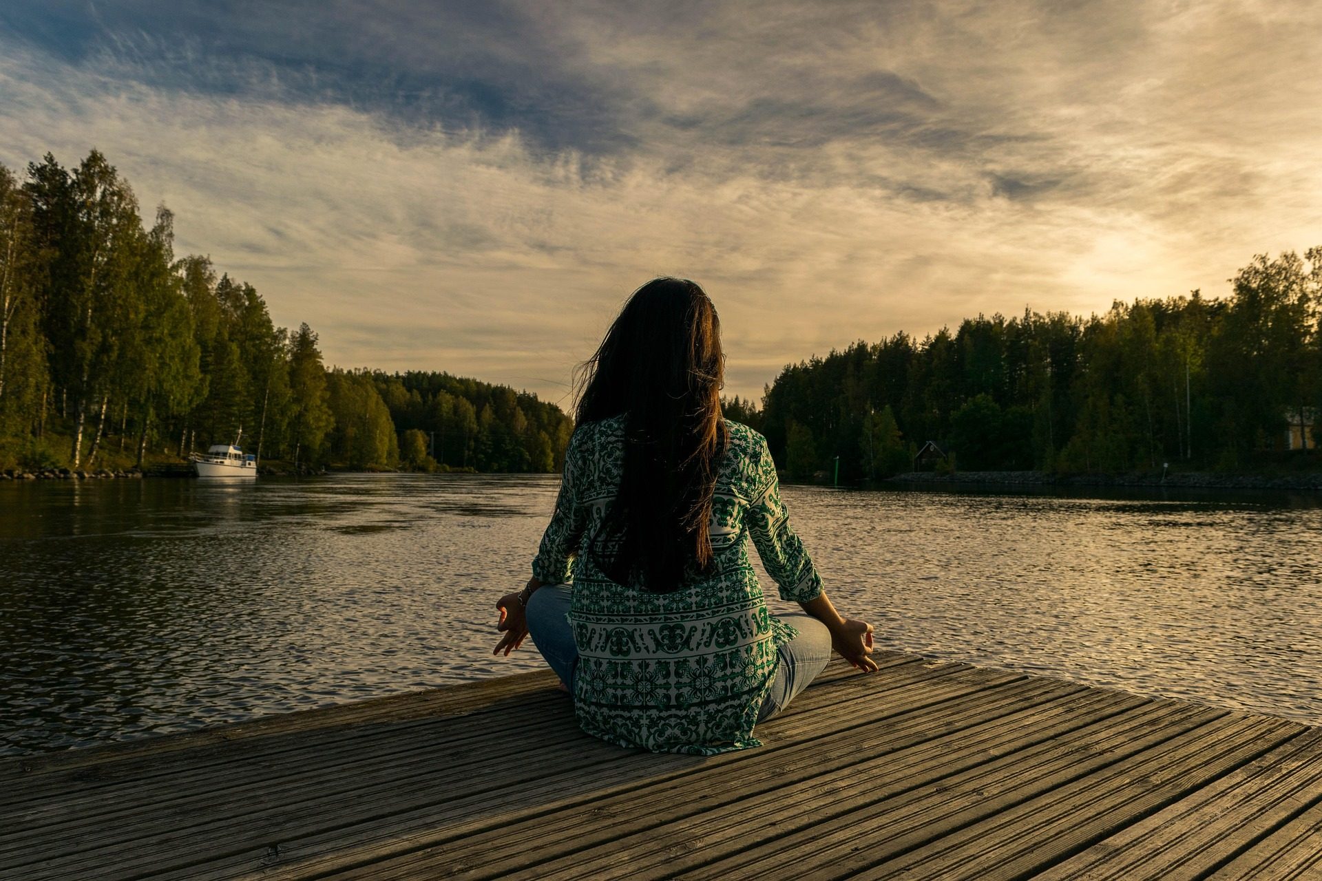 A woman sits in meditation on a lakeside dock at dusk, facing the water