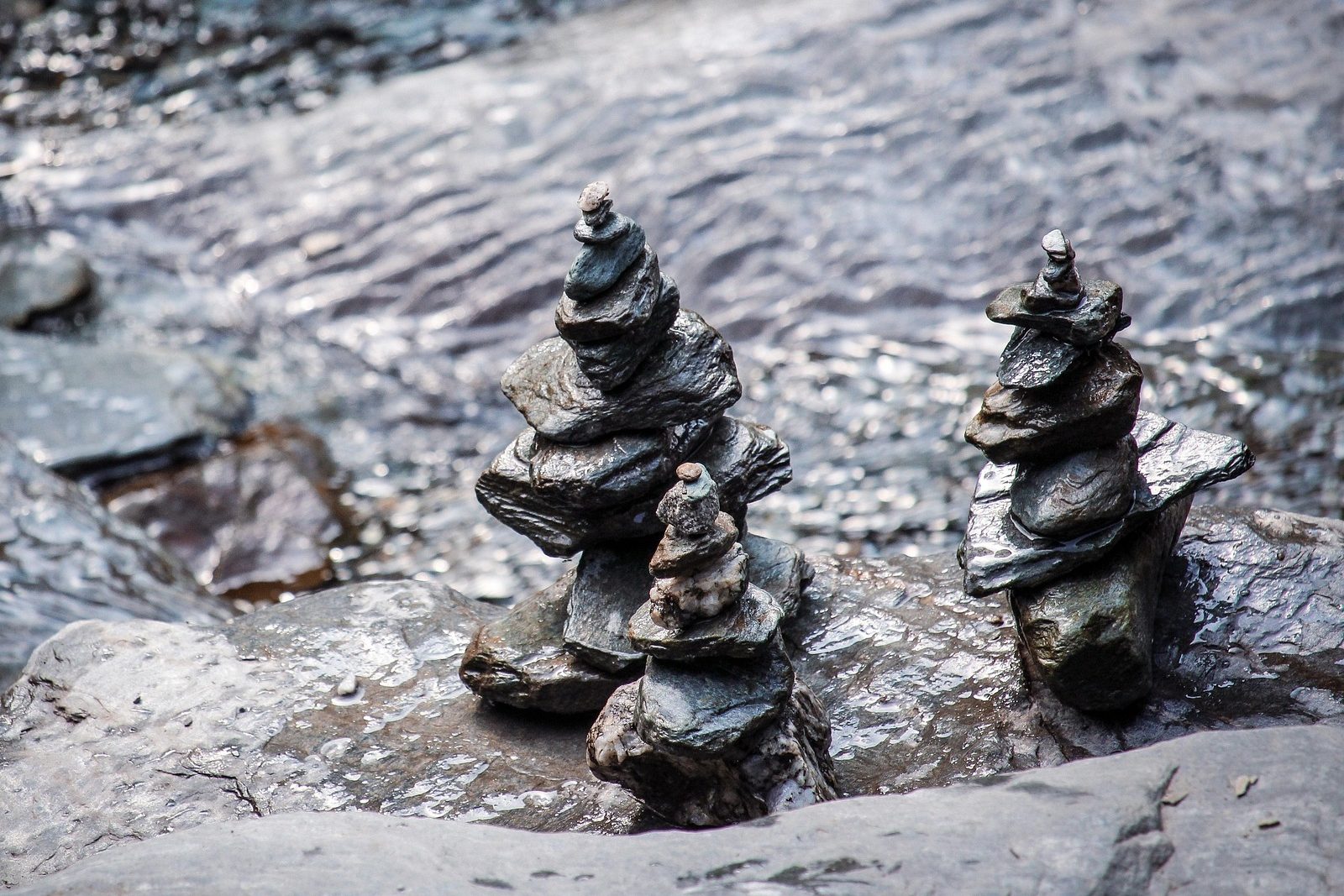 Small stacks of balanced stones on a wet rock beside a running stream