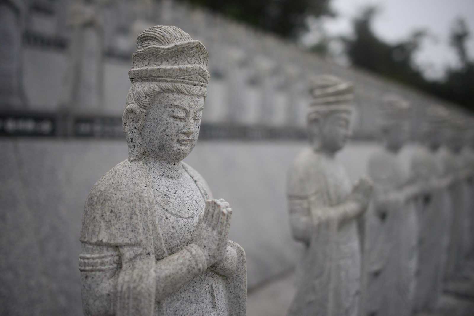 A row of carved stone figures standing with palms pressed together, the nearest one in focus