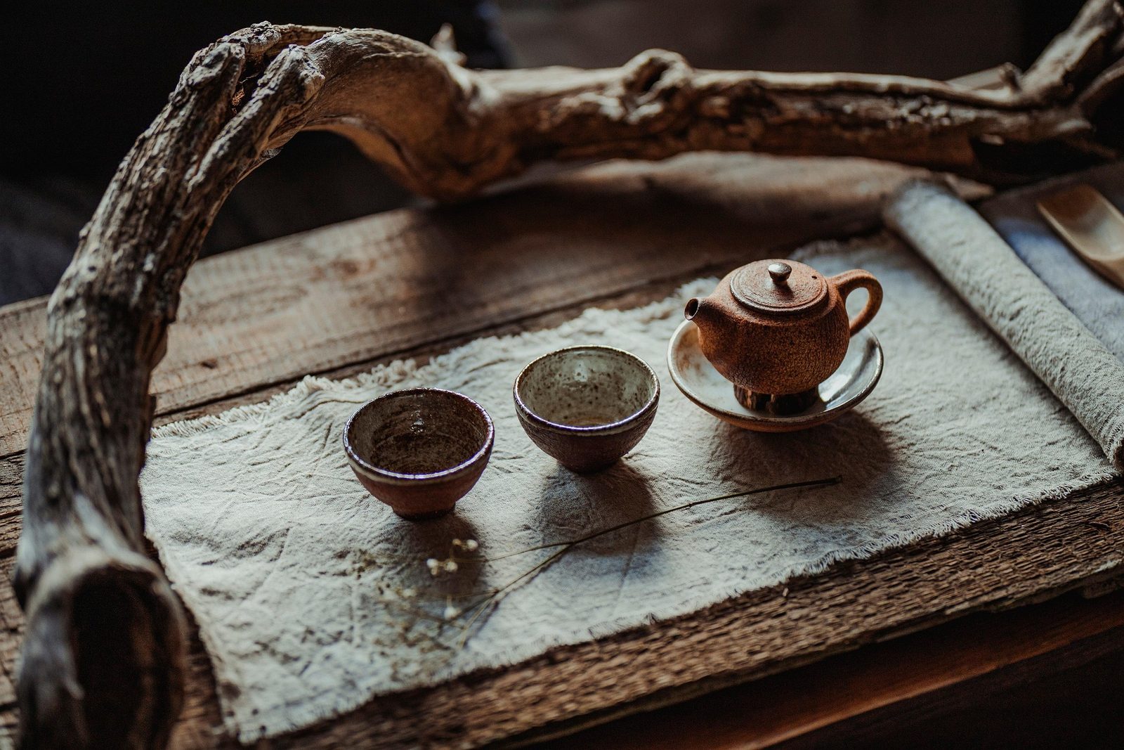 Two small tea bowls and a clay teapot set out on a weathered wooden tray